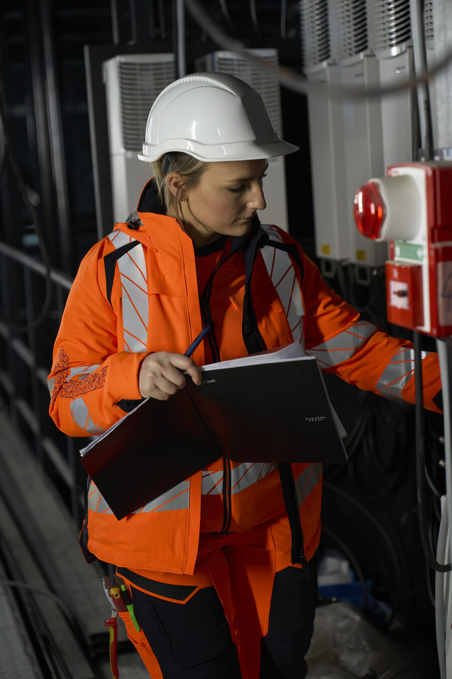 Mitarbeiterin in orangem Warnschutz mit Klemmbrett
